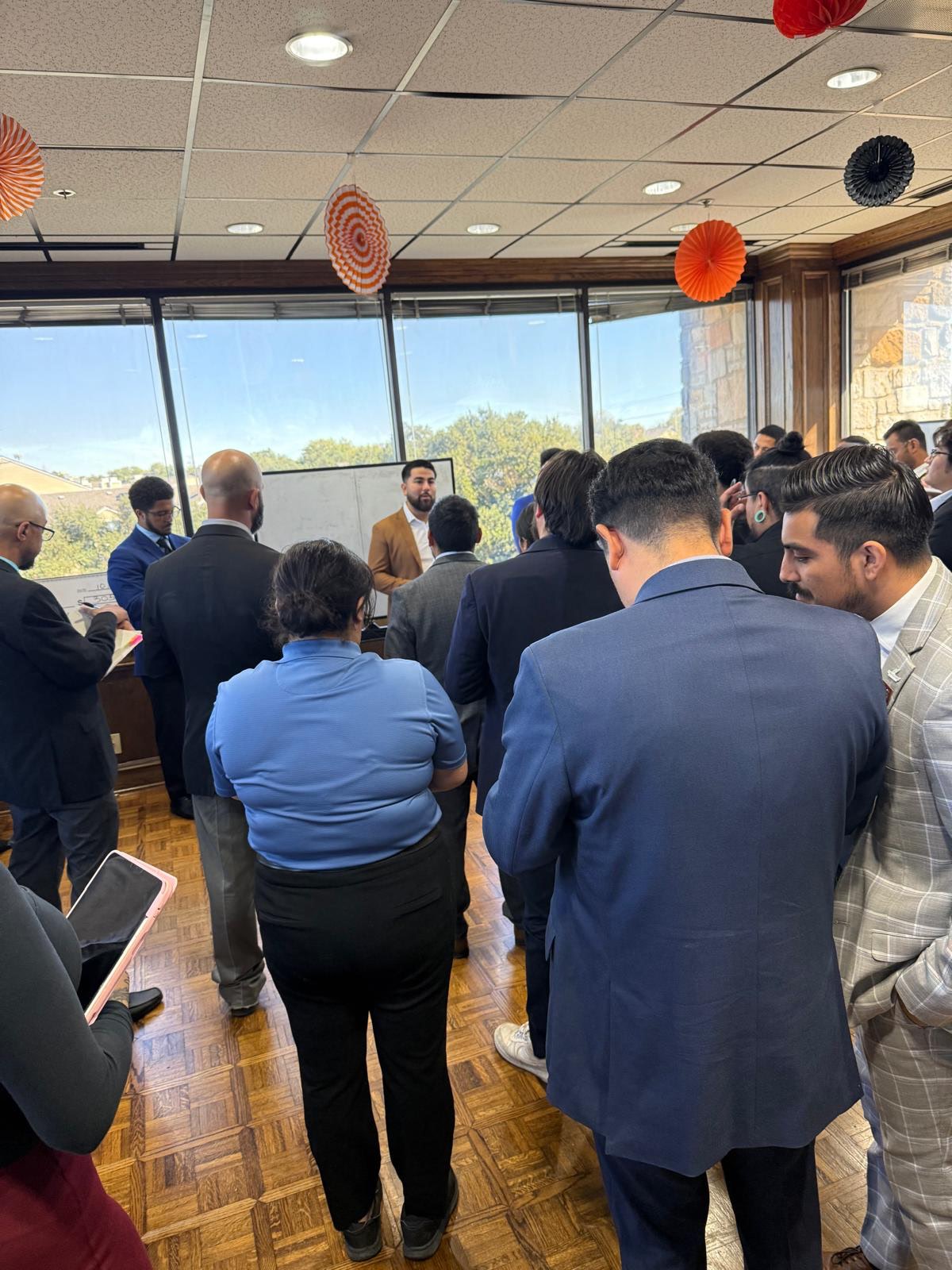 Group of professionals attending a team meeting while a presenter speaks at the front of the room.